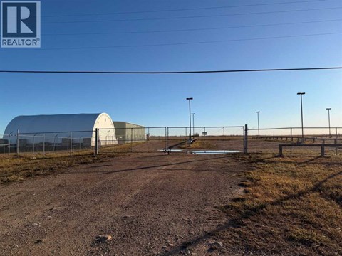 A large building with a grey roof is surrounded by a fence and there are power lines above.