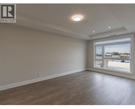 A spacious room with wooden flooring and a large window overlooking a parking lot.