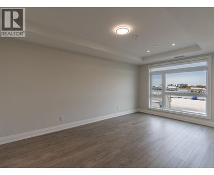A spacious room with wooden flooring and a large window overlooking a parking lot.