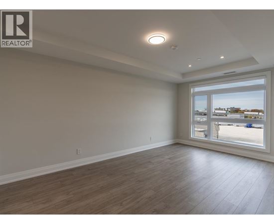 A spacious room with wooden flooring and a large window overlooking a parking lot.