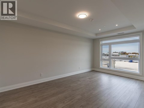 A spacious room with wooden flooring and a large window overlooking a parking lot.