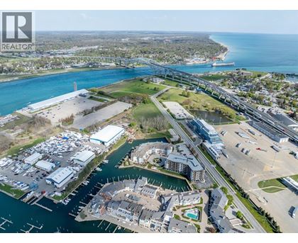 A realtor logo is in the upper left corner of an aerial view of a waterfront area with buildings, boats, and a bridge.