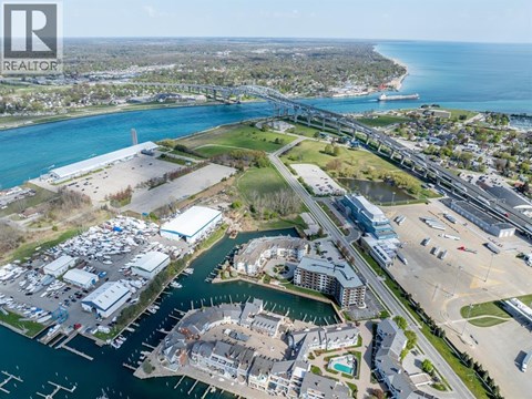 A realtor logo is in the upper left corner of an aerial view of a waterfront area with buildings, boats, and a bridge.