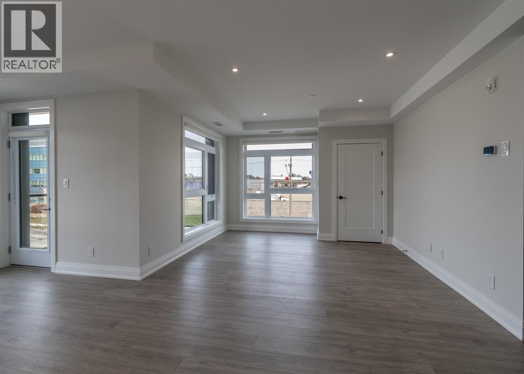 A spacious room with wooden floors and a large window overlooking a parking lot.