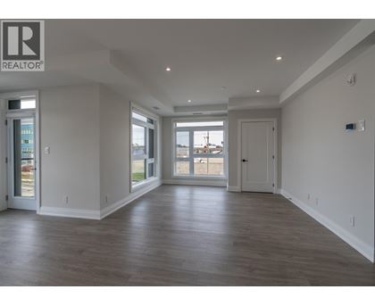 A spacious room with wooden floors and a large window overlooking a parking lot.