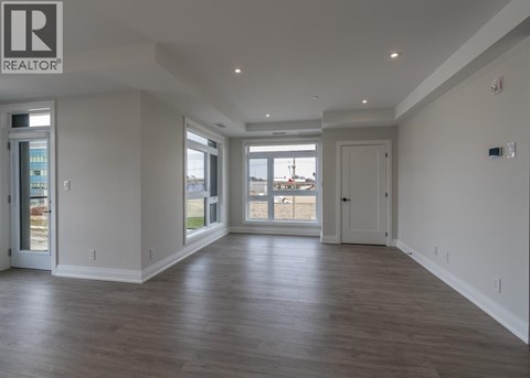 A spacious room with wooden floors and a large window overlooking a parking lot.