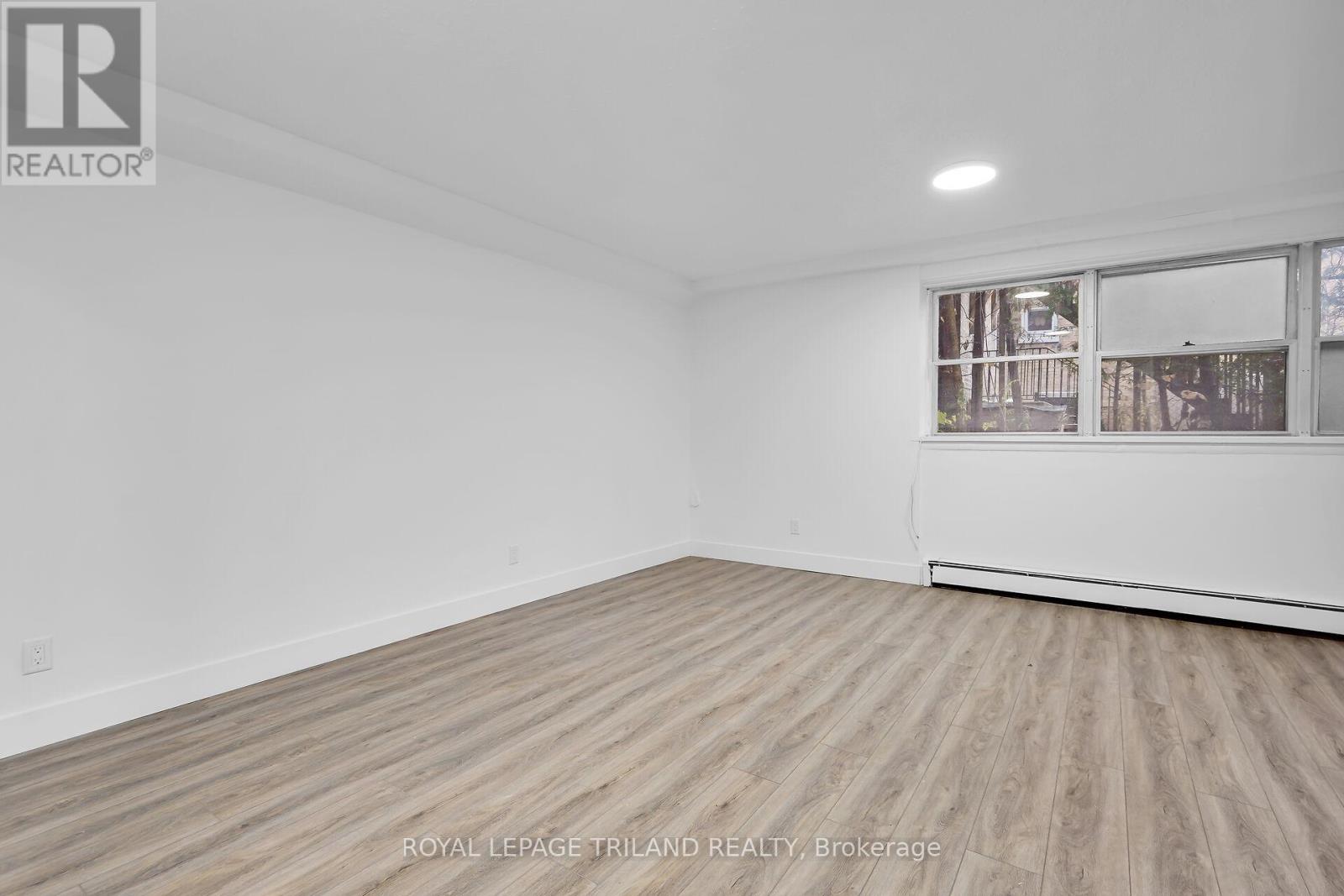 A white room with wooden flooring and a window showing a view of trees.