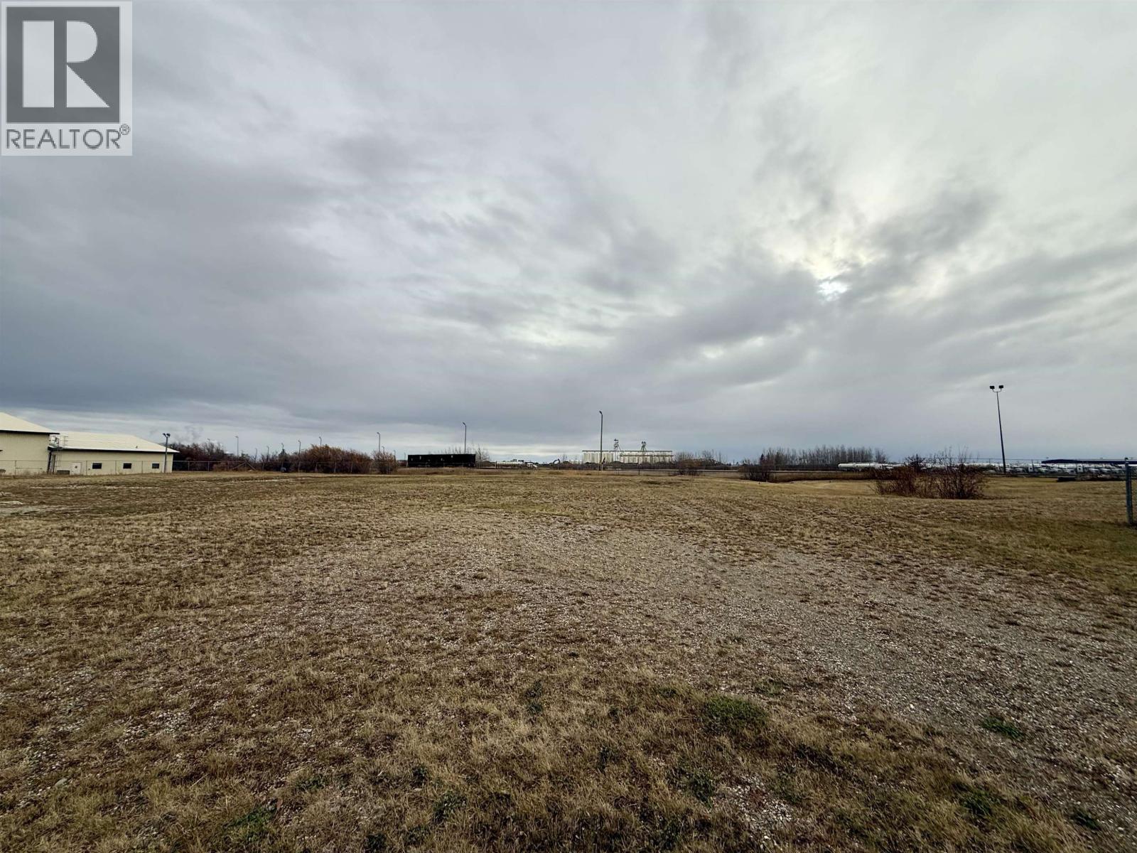 A field with a cloudy sky and a building in the distance.