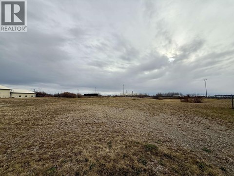 A field with a cloudy sky and a building in the distance.