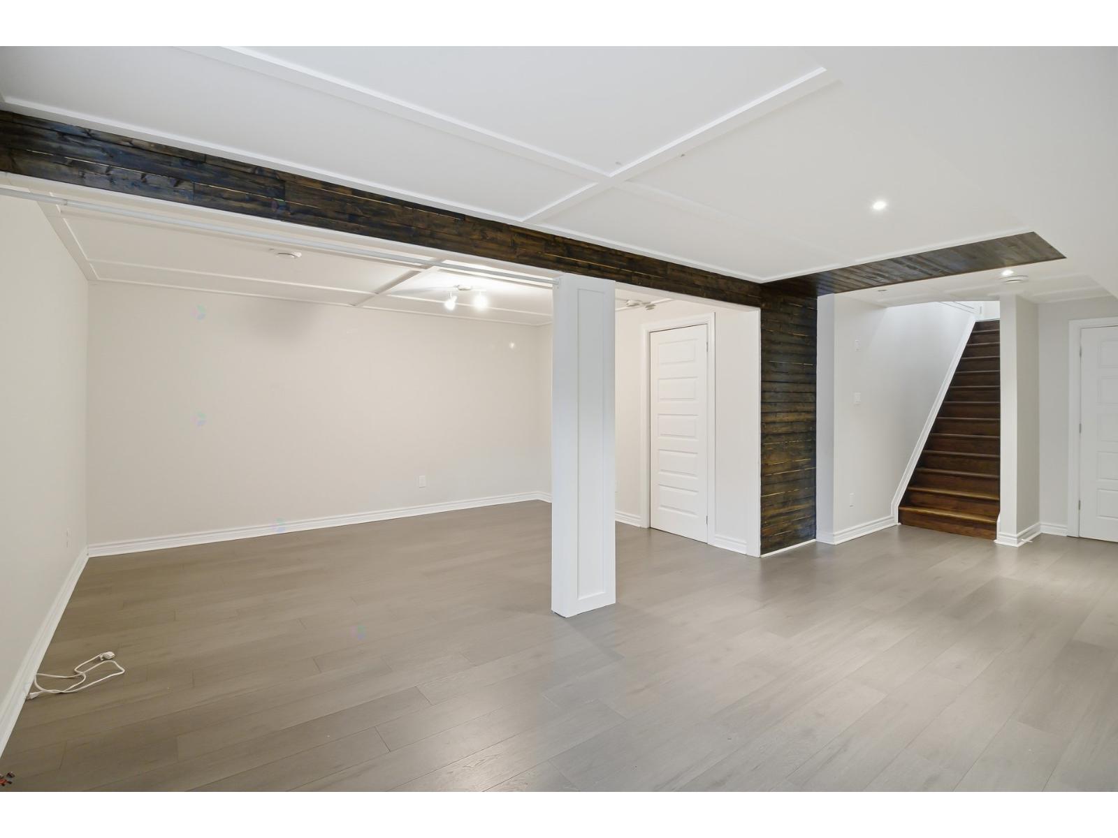 A spacious room with wooden floors and a staircase leading to another room.