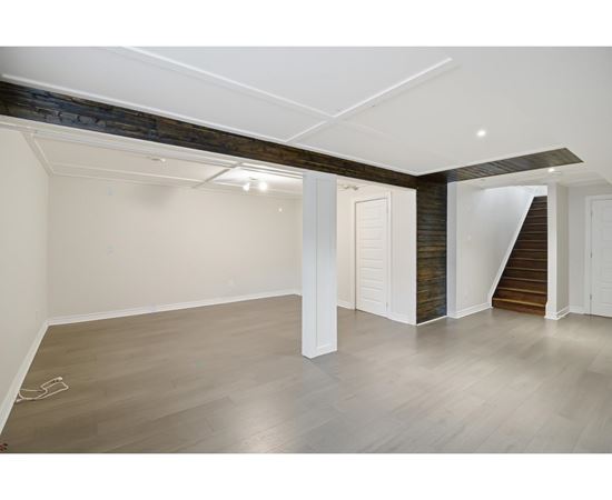 A spacious room with wooden floors and a staircase leading to another room.