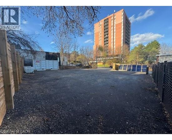 A gravel lot with a fence and a building in the background.