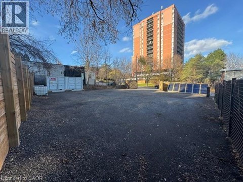 A gravel lot with a fence and a building in the background.