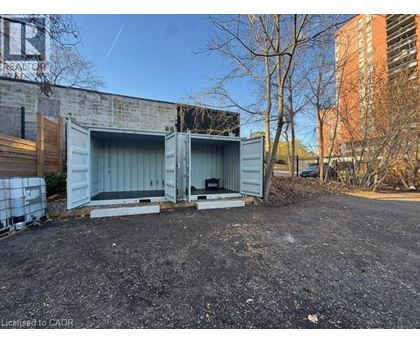 A large grey shipping container sits in a gravel lot.