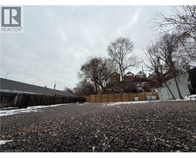 A gravel lot with a fence and houses in the background.
