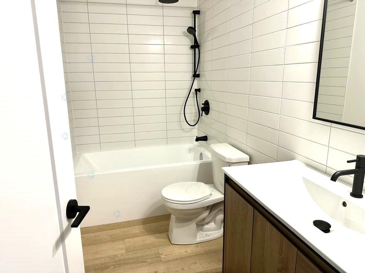 A white toilet is in a bathroom with a white tub and sink.