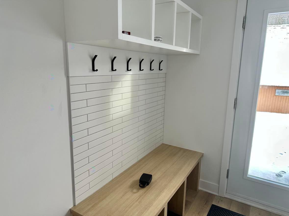 A white tiled wall with a wooden desk and a black object on it.