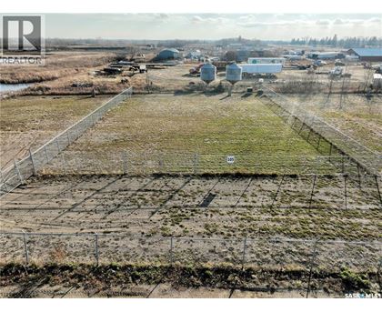 A large open field with a fence in the foreground and buildings in the background.