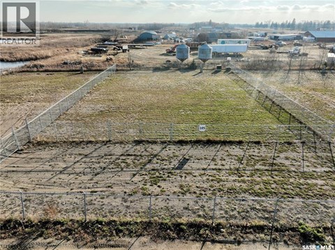 A large open field with a fence in the foreground and buildings in the background.
