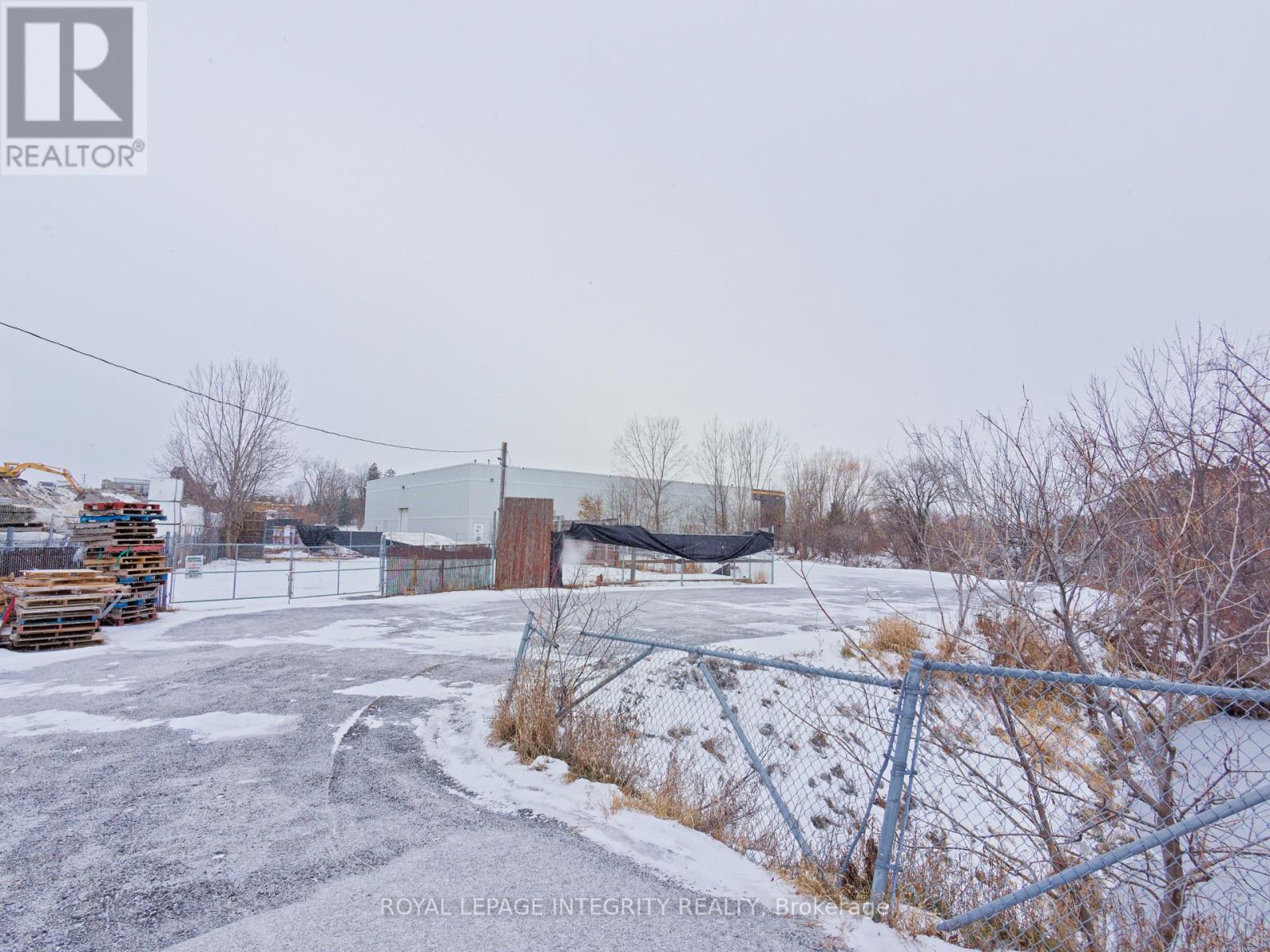 A snowy parking lot with a fence and a building in the background.
