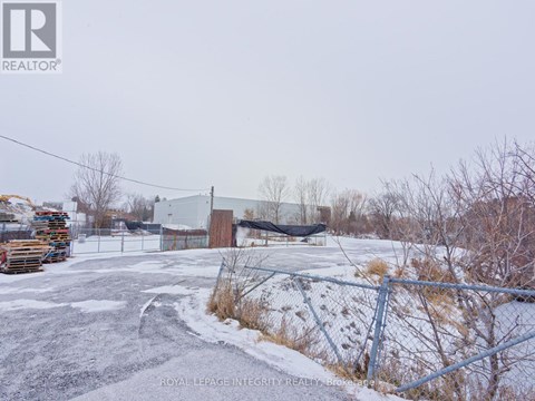 A snowy parking lot with a fence and a building in the background.