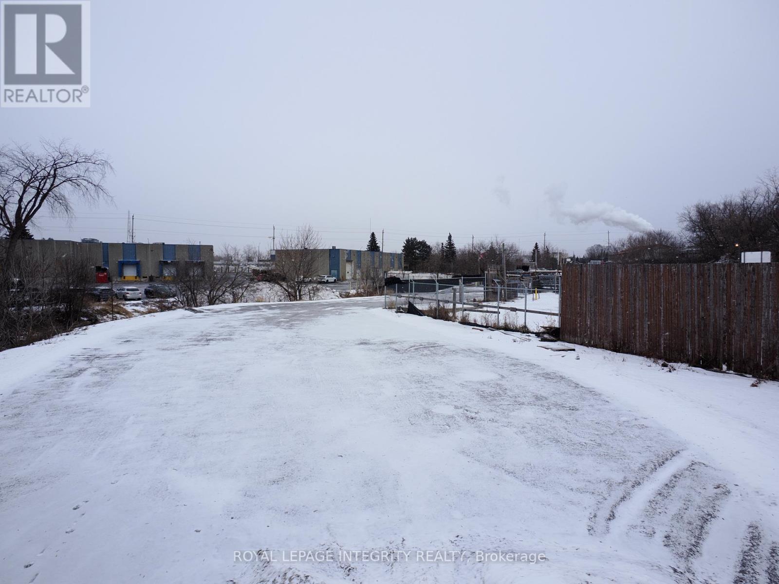 A snow-covered field with a fence on the right side and a building in the background.