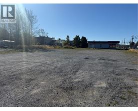 A gravel lot with a building in the background and a logo in the upper left corner.
