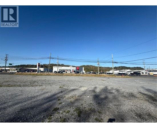 A gravel lot with a building in the background and power lines above.