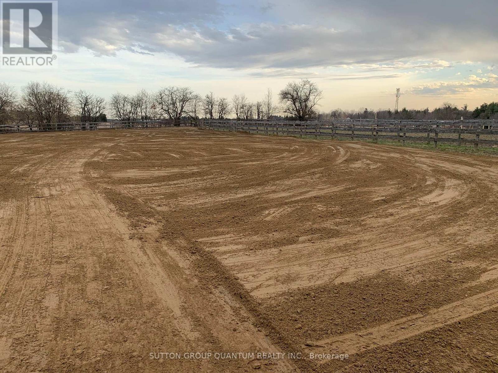 A large, open field with a dirt surface and a fence in the background.
