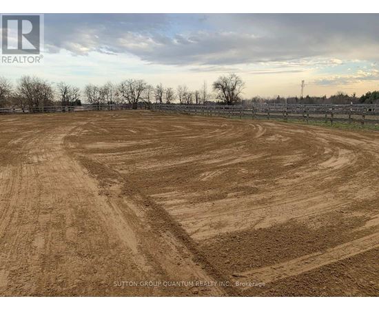 A large, open field with a dirt surface and a fence in the background.