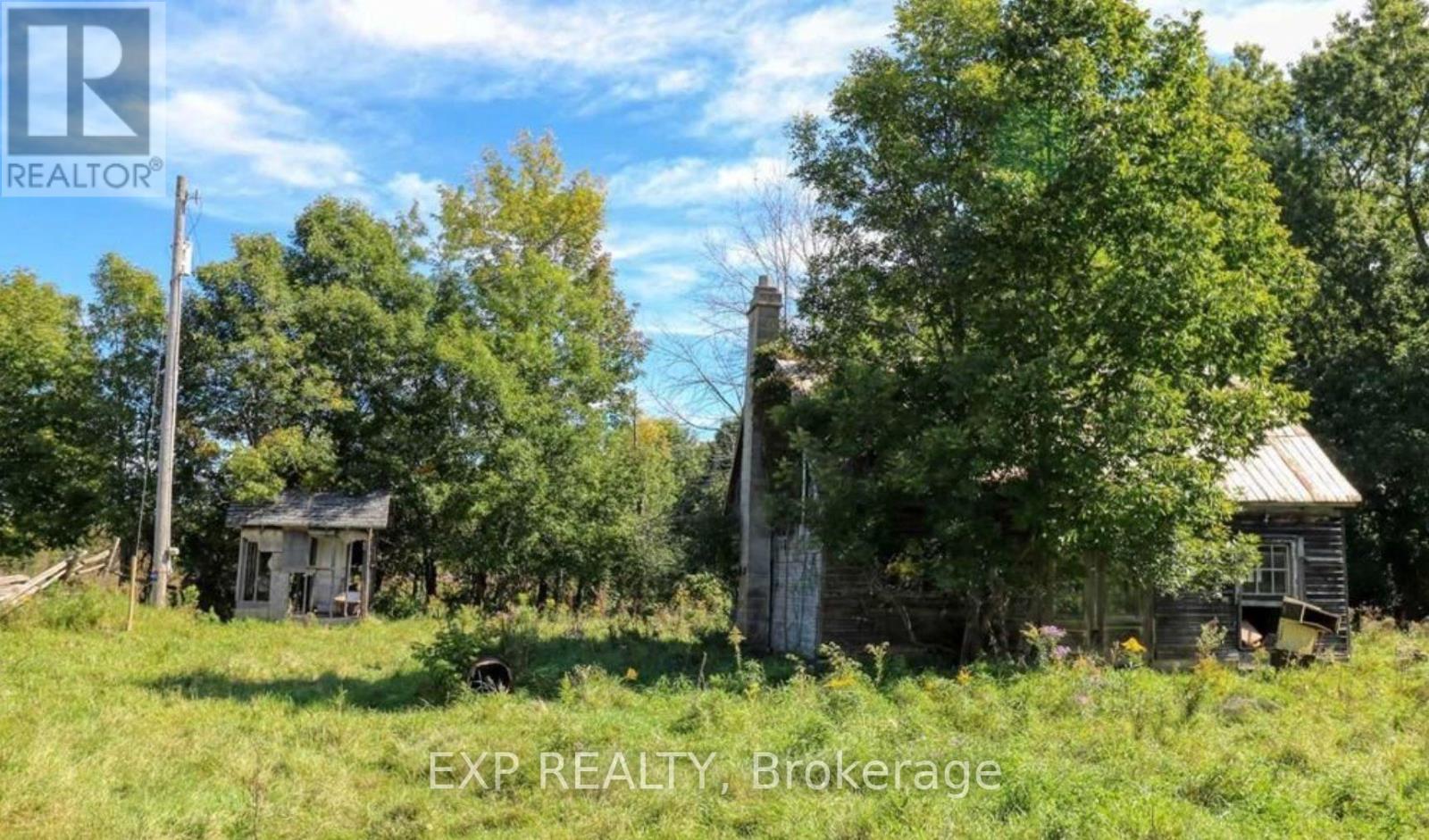 An abandoned house sits in a field with trees around it.