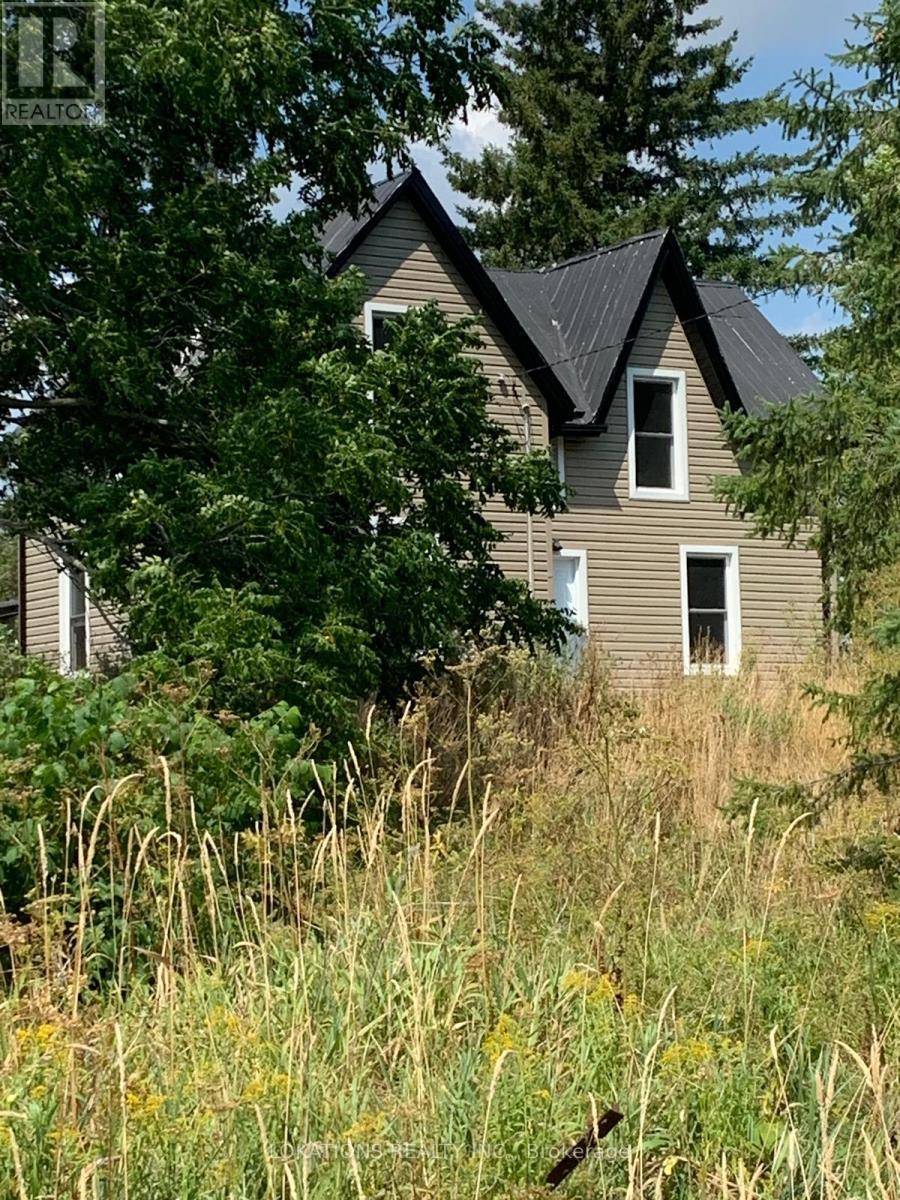 A house with a grey roof and a brown wall is surrounded by greenery.