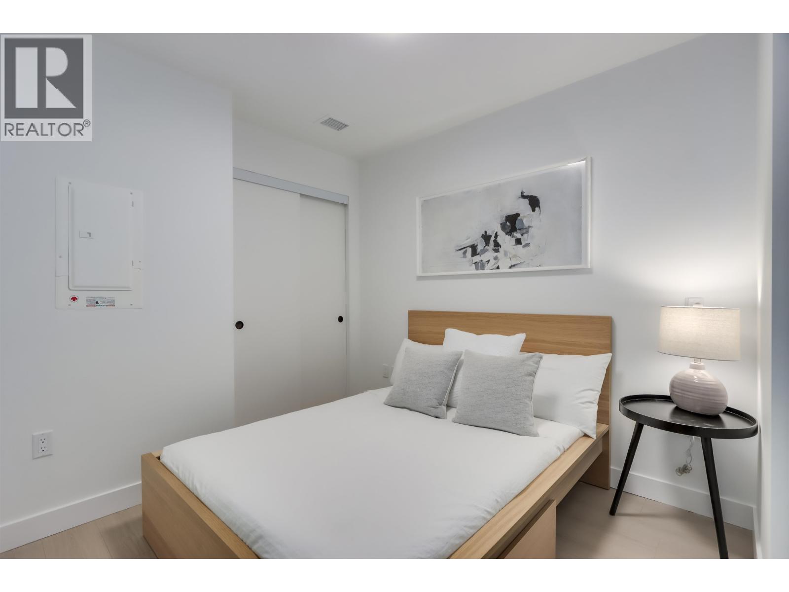 A bedroom with a bed, a small table with a lamp, and a painting on the wall.