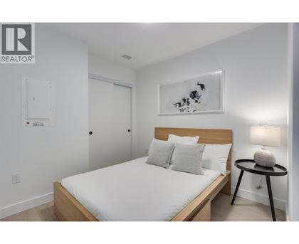 A bedroom with a bed, a small table with a lamp, and a painting on the wall.