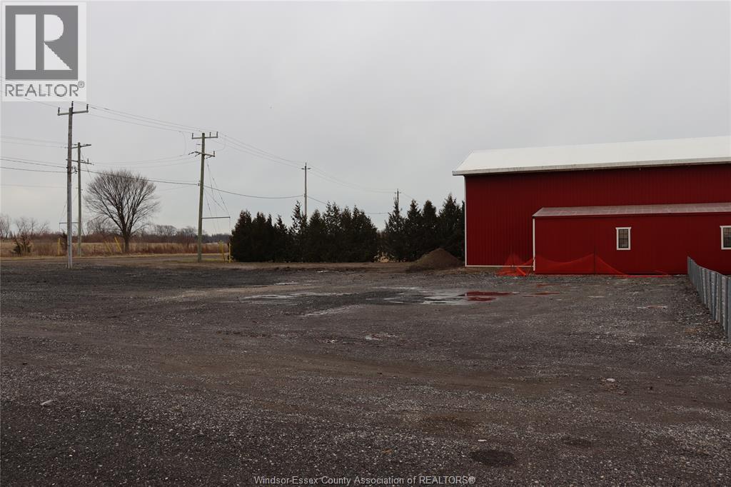 A red barn sits in the middle of a gravel lot.
