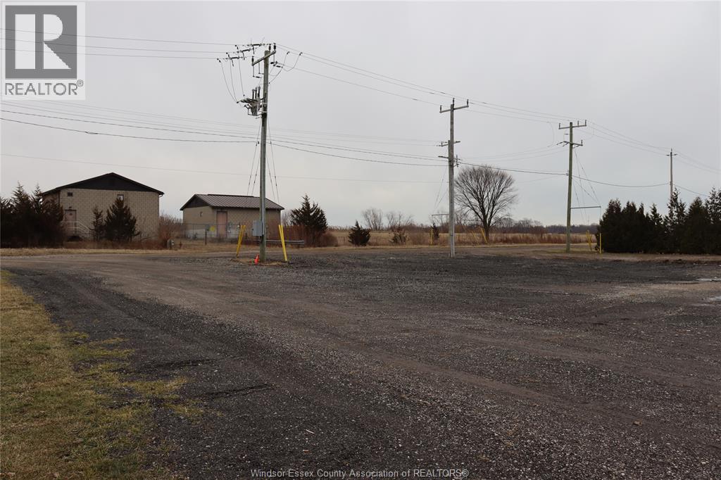 A gravel road with power lines and two houses in the background.
