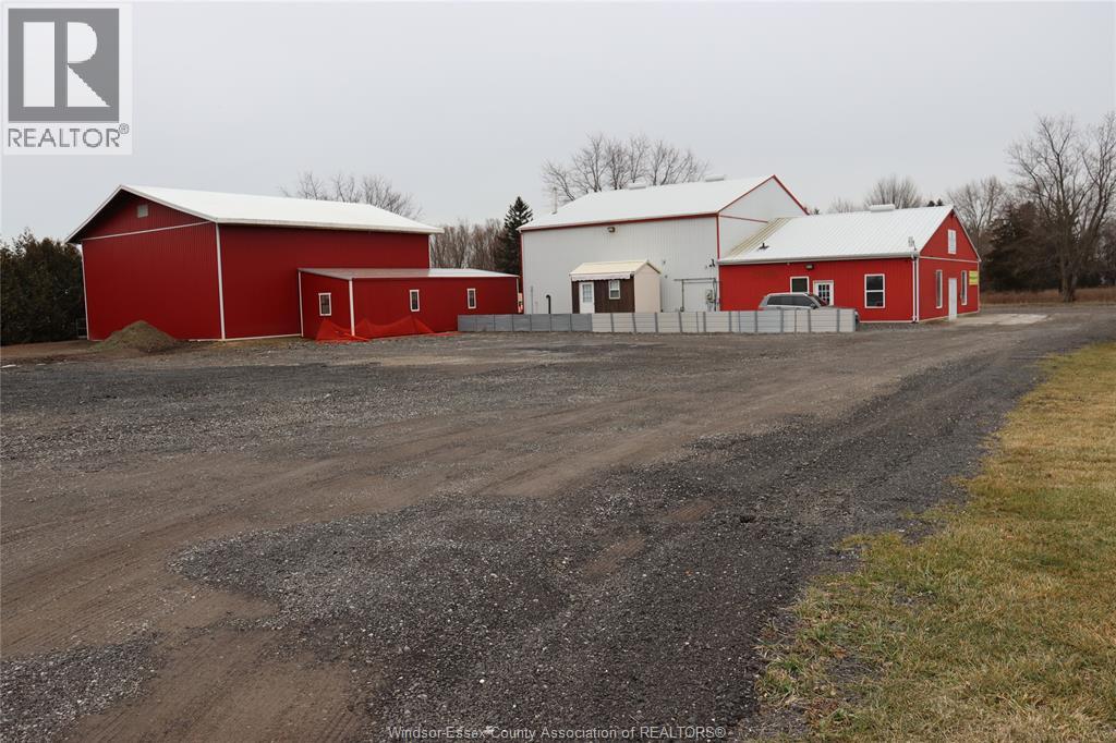A red barn sits next to a white barn with a dirt road in front.