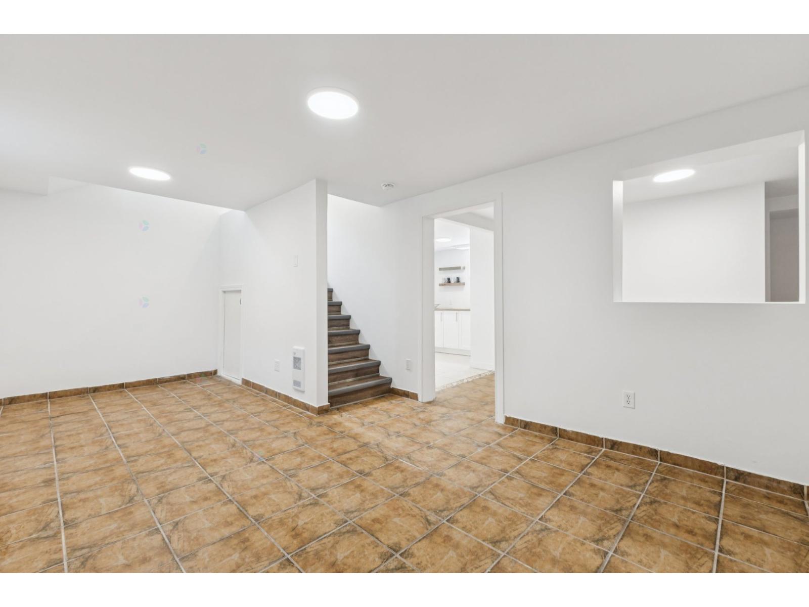 A spacious room with a tiled floor and a staircase leading to another room.