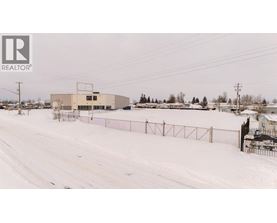 A snowy landscape with a building and a fence in the foreground.