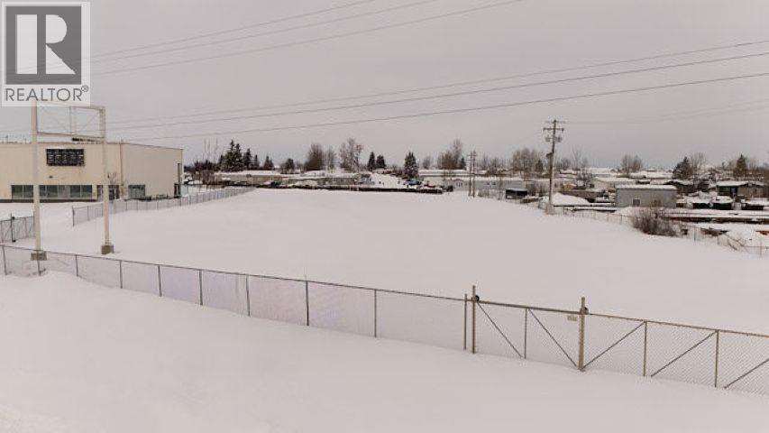 A snowy field with a fence and a building in the background.