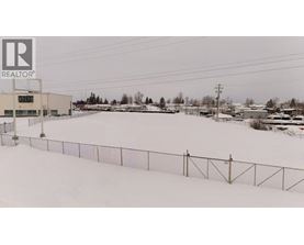 A snowy field with a fence and a building in the background.