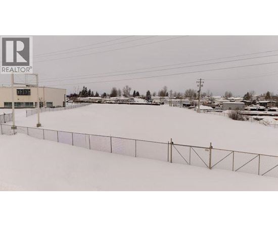 A snowy field with a fence and a building in the background.