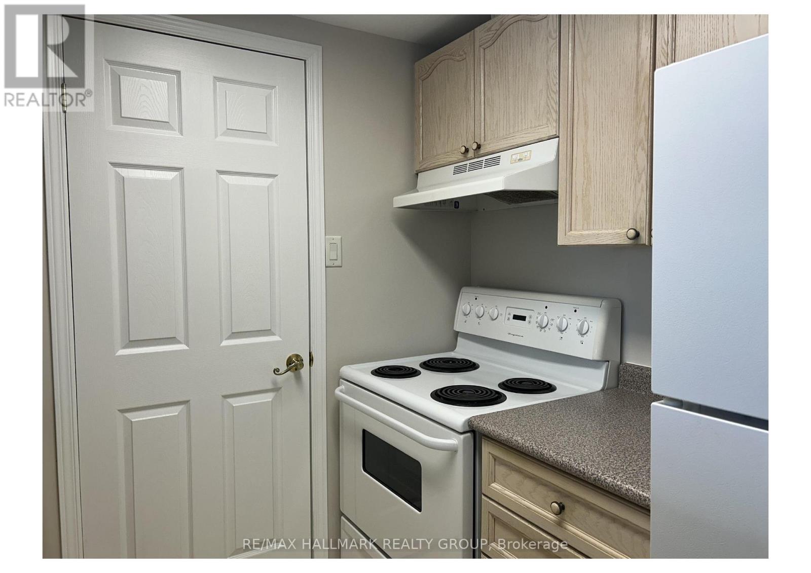 A white door is on the left of a kitchen with a stove and oven.