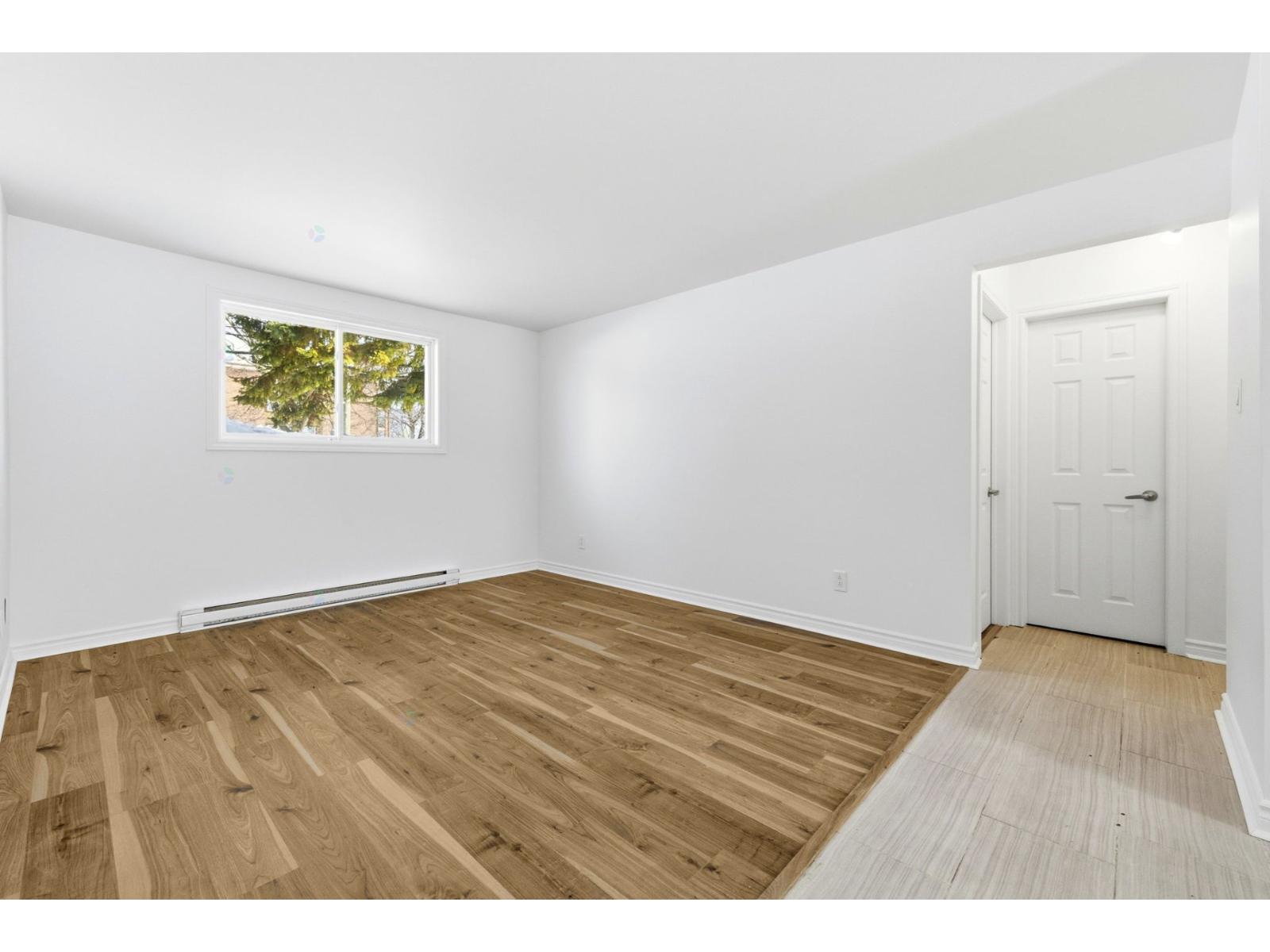 A room with wooden flooring and a window showing trees outside.