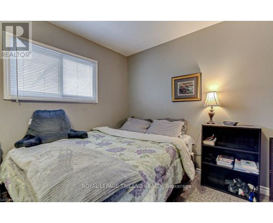 A bedroom with a bed, a nightstand with a lamp, and a bookshelf.