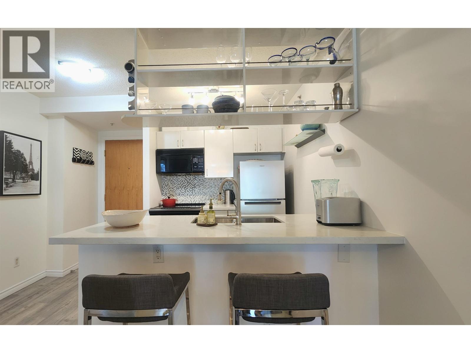A kitchen with a white countertop and two black chairs.