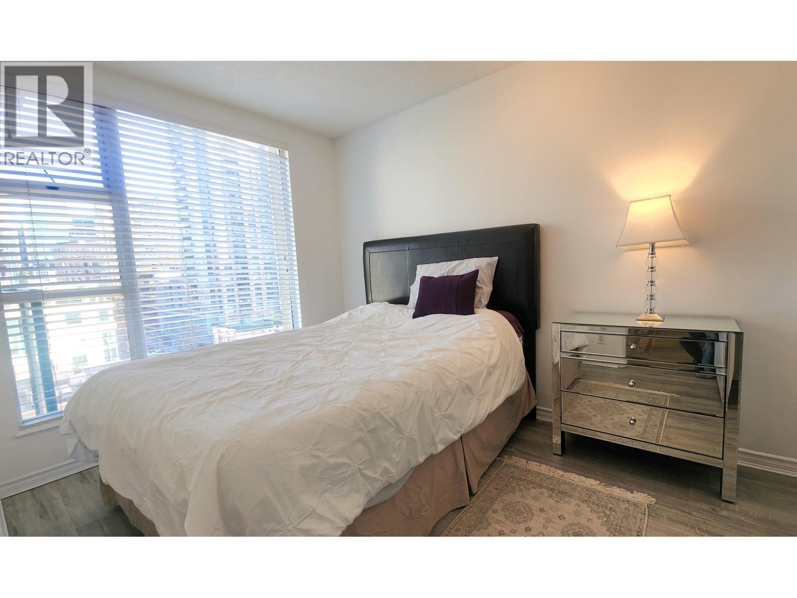 A bedroom with a bed, nightstand, and window.