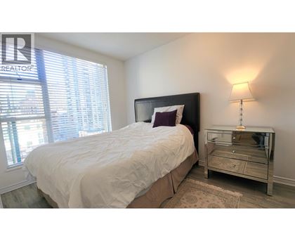 A bedroom with a bed, nightstand, and window.
