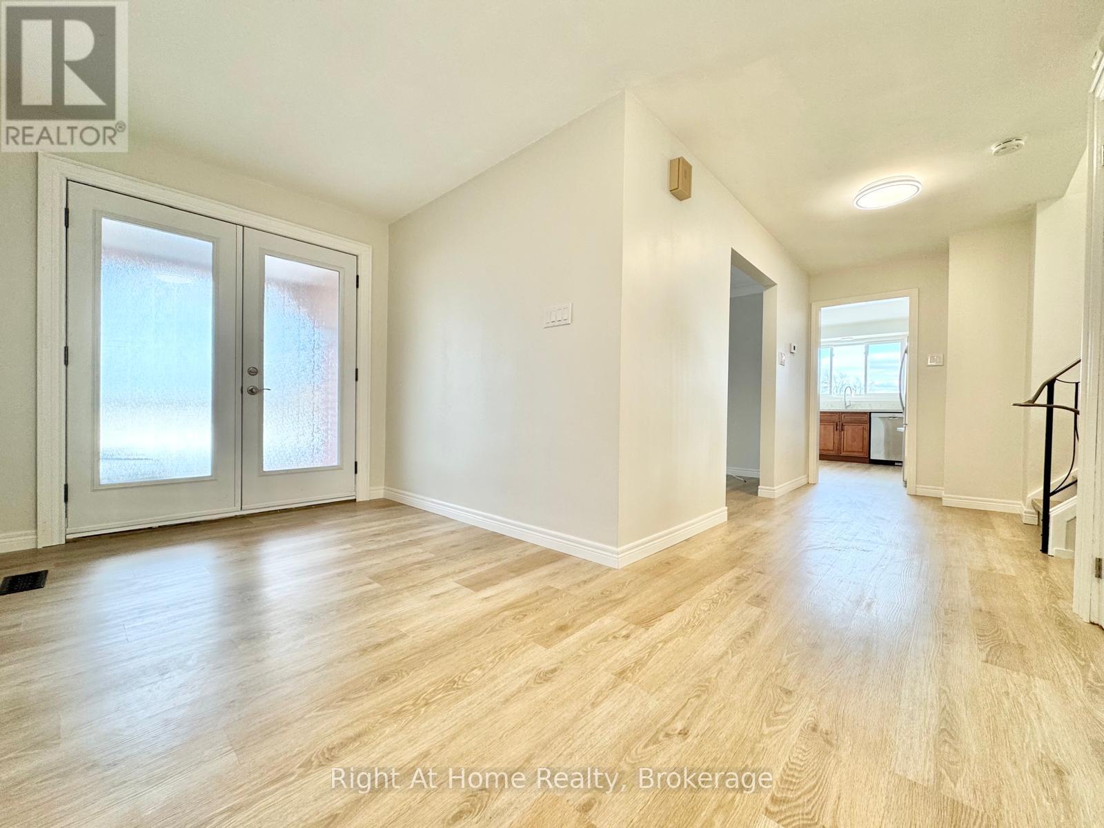 A spacious room with wooden flooring and white walls, featuring a staircase on the right side.