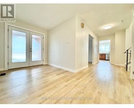 A spacious room with wooden flooring and white walls, featuring a staircase on the right side.